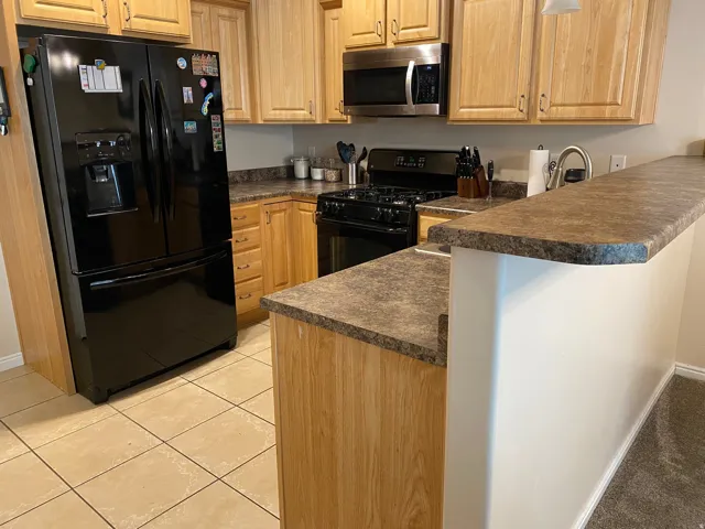 Kitchen featuring light wood cabinetry, stone-look laminate countertops, and tile flooring
