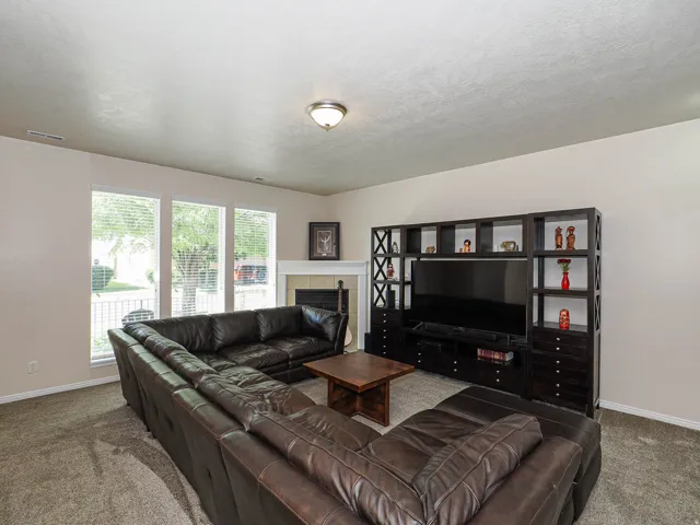 Carpeted living area featuring multiple windows with blinds, a built-in entertainment center, a fireplace with a mantel, and light-toned wall finishes