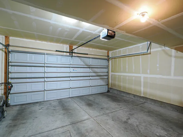 Single-bay garage featuring a panel-style door, concrete flooring, and an exposed ceiling with track for an automatic opener