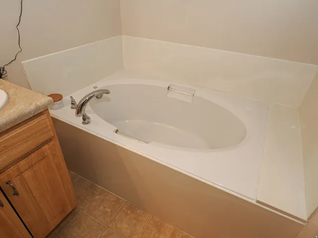 Built-in oval bathtub with deck-mounted chrome fixtures, surrounded by a light-toned enclosure