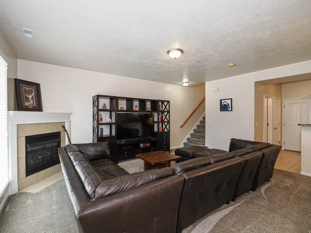 Living area featuring a tiled fireplace with a white mantel, light-toned walls, and grey carpet flooring