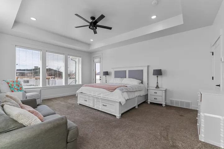 Spacious room featuring broad windows with blinds, recessed lighting, a modern ceiling fan, and tray ceilings