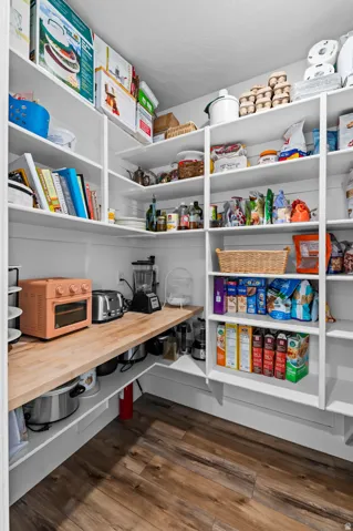 Custom pantry featuring extensive white shelving, a wood-finish countertop, and wood-finish flooring