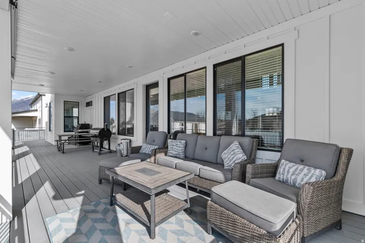 Spacious covered patio featuring a white beadboard ceiling, a durable composite deck, and dark-framed windows
