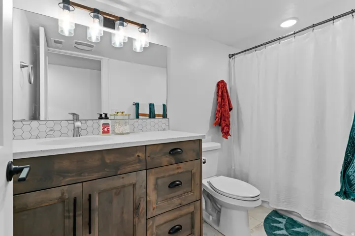 Bathroom featuring a wood-finish vanity with dark hardware, a white countertop, and a hexagonal tile backsplash