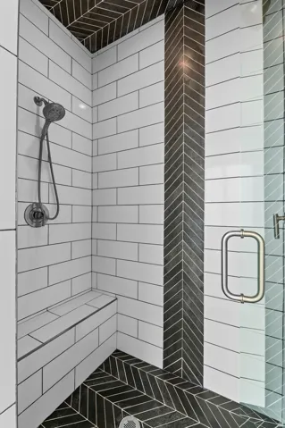 Shower featuring white subway tile walls, a built-in bench, black herringbone floor tile, a black herringbone accent column, and a glass shower door with a polished chrome handle