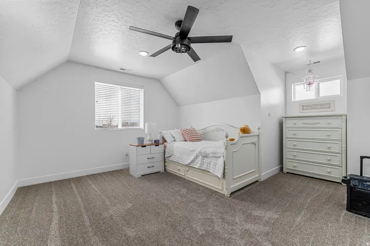 Attic space featuring sloped ceilings, textured white walls, and gray carpet flooring