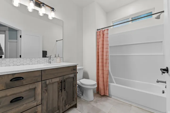 Contemporary bathroom featuring a wood-finish vanity with dark hardware, a white countertop, and a hexagonal tile backsplash