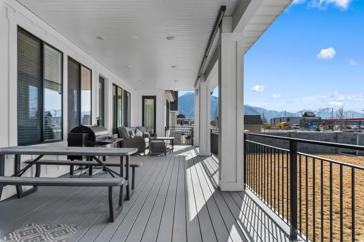 Expansive covered deck featuring composite flooring, white paneled ceiling, recessed lighting, and black metal railing