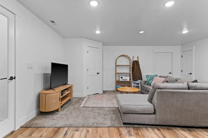 Open living area featuring recessed lighting, a combination of wood-finish flooring and carpeting, and multiple white paneled doors with black hardware