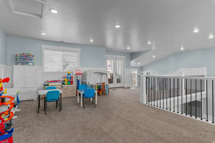 Spacious carpeted room featuring light blue walls with white wainscoting, recessed lighting, and a white window with blinds