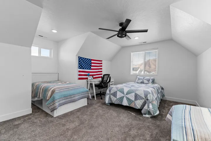 Carpeted bedroom with vaulted ceilings, a ceiling fan, and multiple windows providing natural light