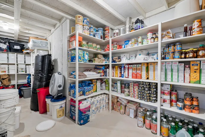 Extensive storage area featuring white built-in shelving, exposed ceiling beams, and concrete flooring