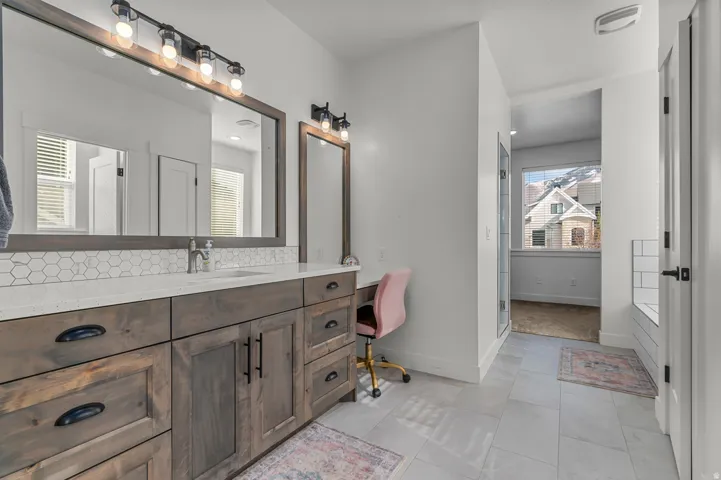 Double vanity featuring wood-finish cabinetry, white countertops, and hexagon tile backsplash