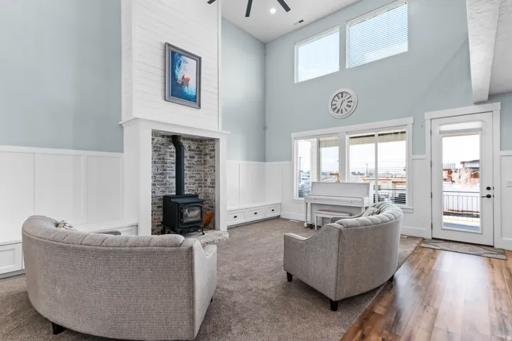 Vaulted ceiling living space with a shiplap fireplace surround featuring a wood-burning stove, built-in bench seating, wood-finish flooring, and large windows