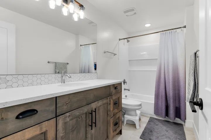 Bathroom featuring a spacious wood-finish vanity with a light-toned countertop, an integrated sink, and a hexagonal tile backsplash