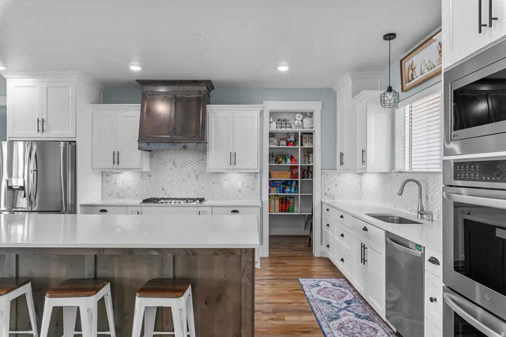 Spacious kitchen featuring an expansive island with wood-finish paneling, white shaker cabinetry, stainless steel appliances, and a hexagon tile backsplash