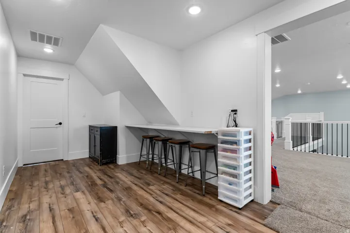 Versatile loft area featuring wood-finish flooring, a built-in counter surface, recessed lighting, and a solid core door