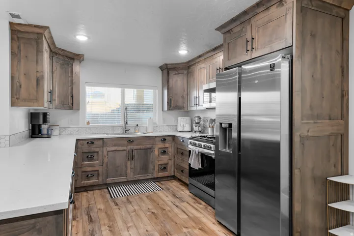Kitchen featuring wood-finish cabinetry, stainless steel appliances, a white solid surface countertop, and wood-finish flooring