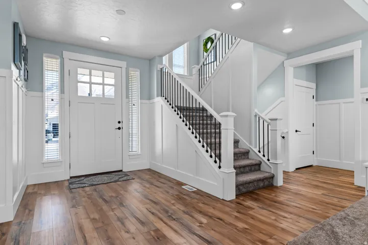 Spacious entry featuring wood-finish flooring, white board and batten wall details, and a staircase with wrought iron balusters