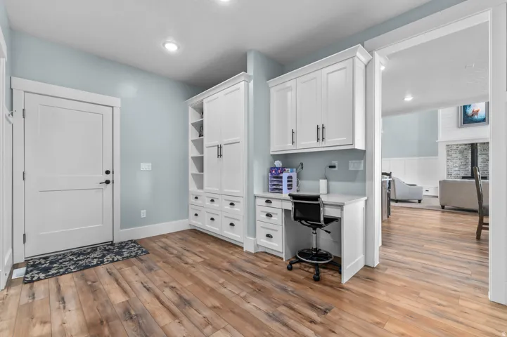 Entryway featuring wood-finish flooring, a white paneled door, recessed lighting, and a built-in desk with overhead cabinetry