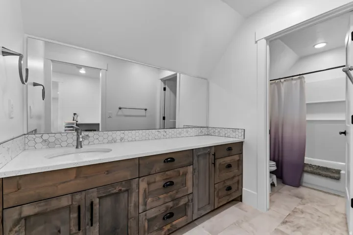 Bathroom vanity featuring a quartz countertop, integrated sink, and wood-finish cabinetry with dark hardware