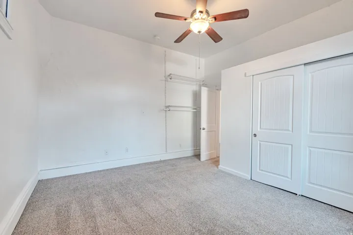 Carpeted room with white walls, wood-finish ceiling fan, and white sliding closet doors