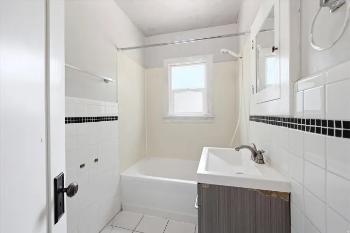 Bathroom featuring a white bathtub, ceramic wall tiling with a black accent strip, and a window