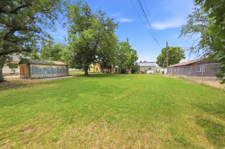 Expansive grassy lot featuring mature trees and a chain-link fence