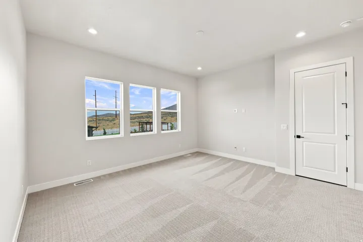 Spacious room featuring light gray carpet, multiple recessed ceiling lights, white interior door with black hardware, and three large windows