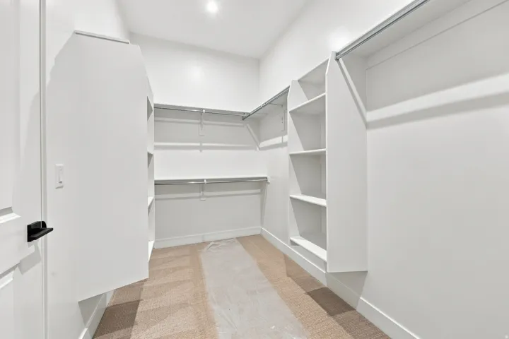 Expansive walk-in closet featuring built-in shelving, multiple hanging rods, and recessed lighting