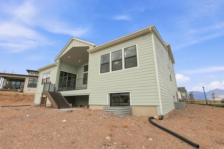 Exterior featuring light green siding, multiple large windows, a covered patio with recessed lighting, and an outdoor staircase with metal railings