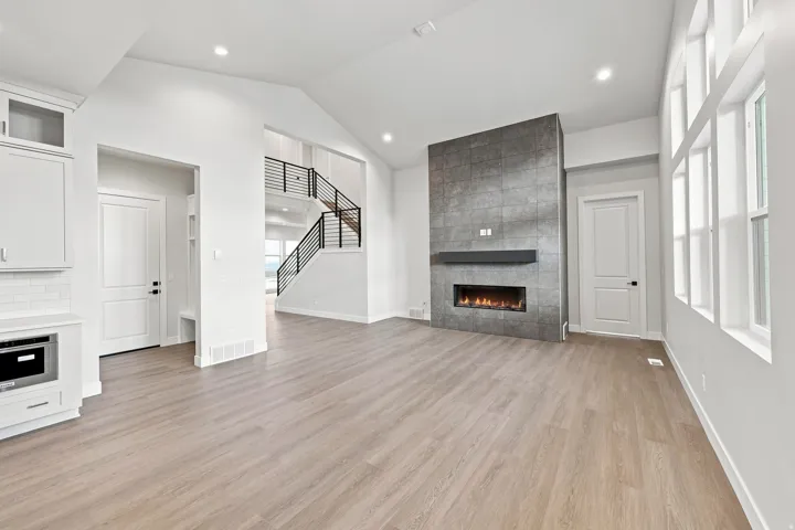 Vaulted ceilings, wood-finish flooring, a modern fireplace with a dark tile surround, and a contemporary staircase with metal railings