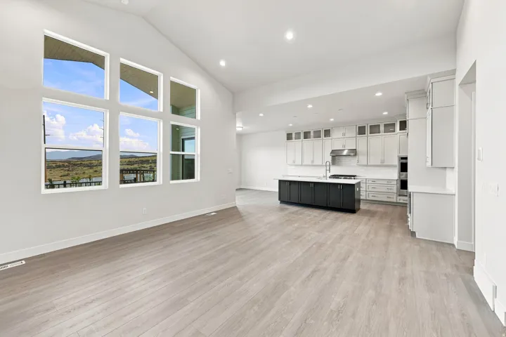 Vaulted ceiling, expansive windows, wood-finish flooring, recessed lighting, and a kitchen featuring a central island with countertop seating