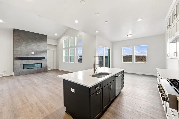 Open-concept living space with vaulted ceilings, a contemporary electric fireplace with a tiled surround, wood-finish flooring, and an expansive kitchen island with a built-in sink and dishwasher