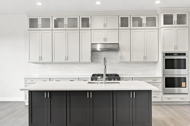 Kitchen featuring white shaker cabinetry, glass-front upper cabinets, a dark kitchen island with stone countertop, stainless steel double wall ovens, and wood-finish flooring