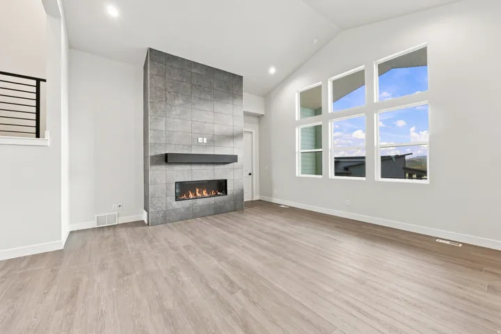 Vaulted ceiling, floor-to-ceiling tiled fireplace, linear electric fireplace, wood-finish flooring, and expansive window wall