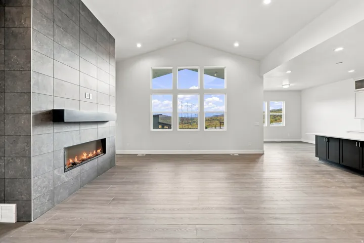 Vaulted ceilings, a tile-clad fireplace with a linear insert, wood-finish flooring, and expansive windows showcasing a distant landscape