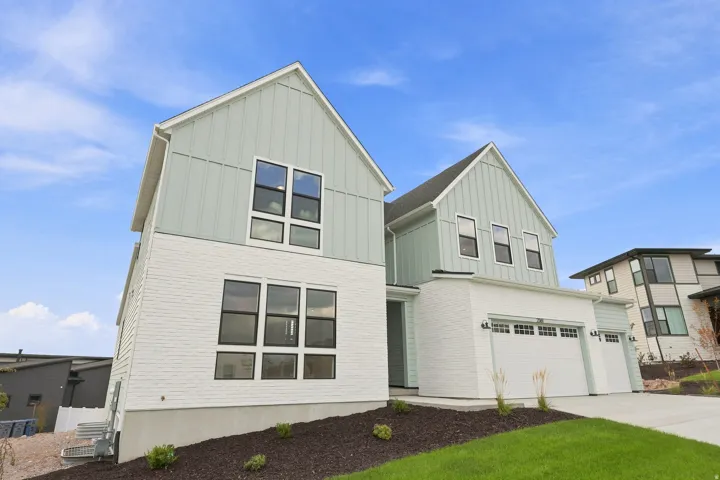 Contemporary exterior with light green vertical siding and white brick, featuring large black-framed windows, a two-car garage, and a single-car garage