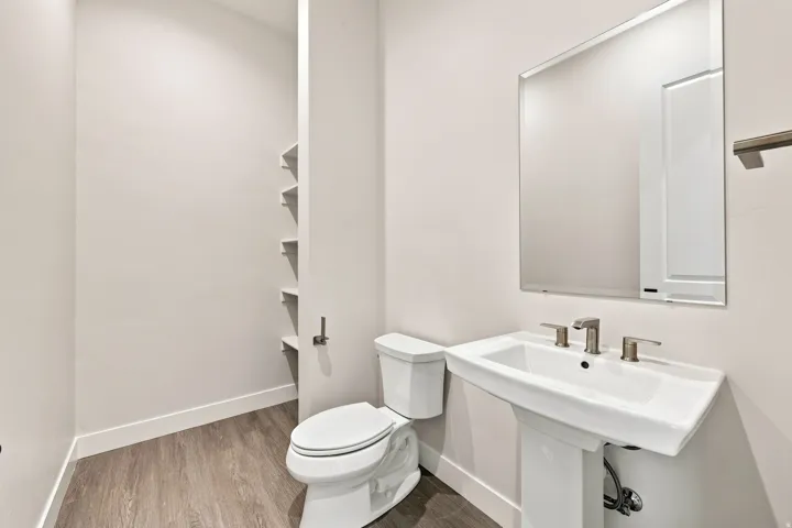 Pedestal sink with brushed nickel faucet, wall-mounted mirror, wood-finish flooring, and integrated wall shelving