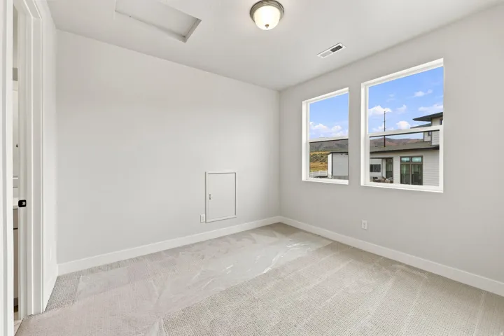 Neutral wall paint, two single-hung windows, flush mount ceiling light fixture, light gray carpeting, and white trim