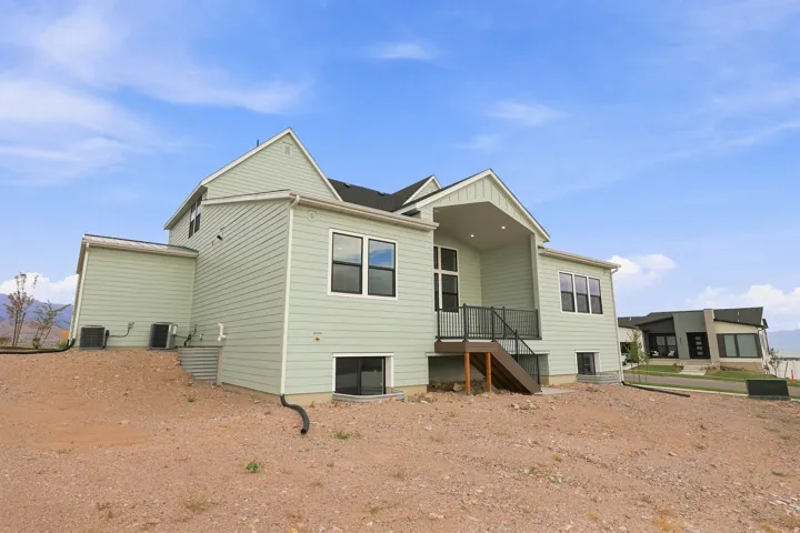 Light green siding exterior with a covered deck, dark framed windows, and a partially exposed lower level