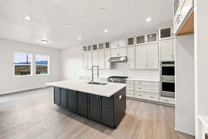 Spacious kitchen featuring an expansive island with a sink, stainless steel appliances, white cabinetry, and wood-finish flooring