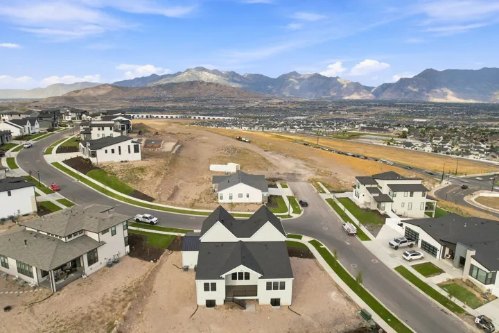 Modern residential development featuring a newly constructed home with a dark shingle roof, light-colored siding, and structured landscaping
