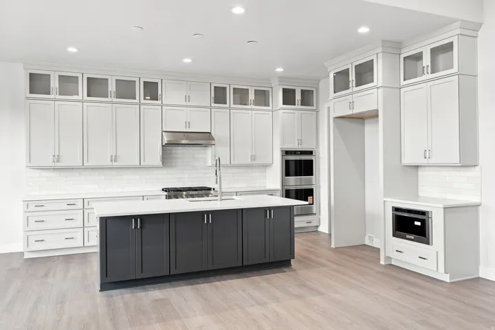 Contemporary kitchen featuring recessed lighting, a two-tone island with a stainless steel faucet, light wood-finish flooring, and white cabinetry with glass upper doors