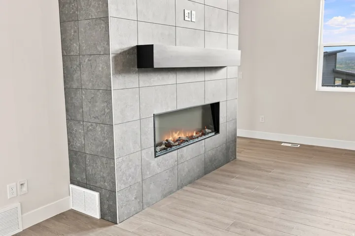 Floor-to-ceiling tile fireplace featuring a built-in electric firebox, a floating mantel, and wood-finish flooring