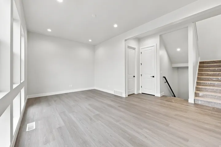 Recessed lighting illuminates wood-finish flooring and multiple windows with white trim