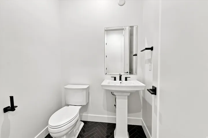Pedestal sink with a matte black faucet, wall-mounted mirror, and herringbone pattern flooring