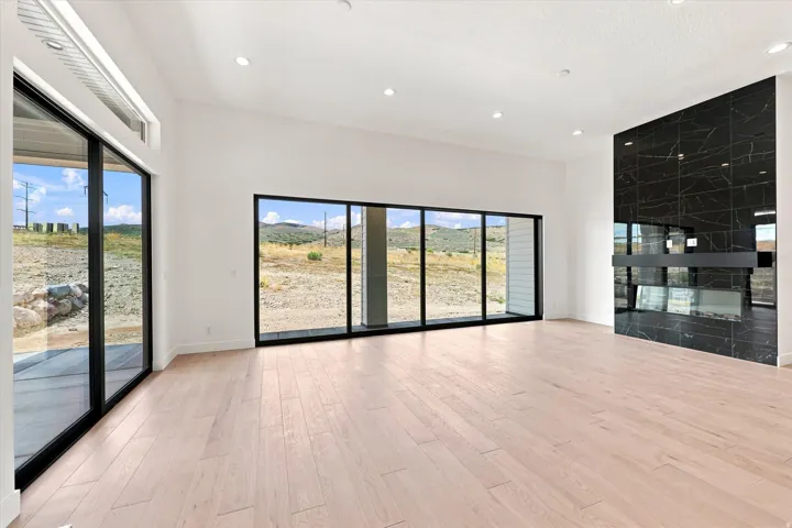 Expansive room featuring multiple full-height windows, a prominent black stone-tiled fireplace, light wood-finish flooring, and recessed ceiling lighting