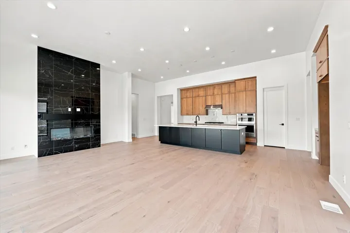 Open-concept living space featuring wide-plank wood-finish flooring throughout, recessed ceiling lighting, and a custom kitchen island with black cabinetry